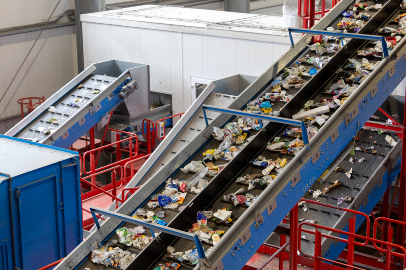 Inclined conveyor belts carrying mixed plastic waste through a recycling sorting facility